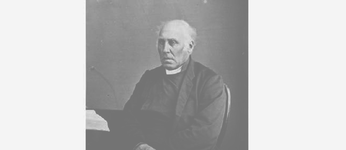 Image: Black and white photograph of seated elderly man wearing a clerical collar