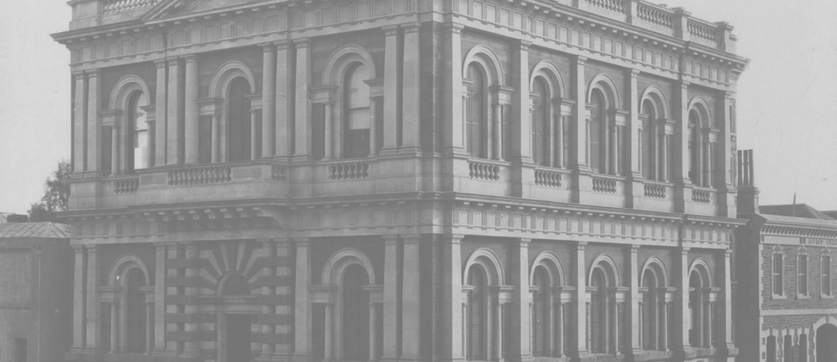 Image: Black and white photograph of a two storied stone building featuring arched windows