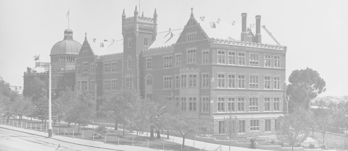 Image: A large stately building made of brick fronted by a large street