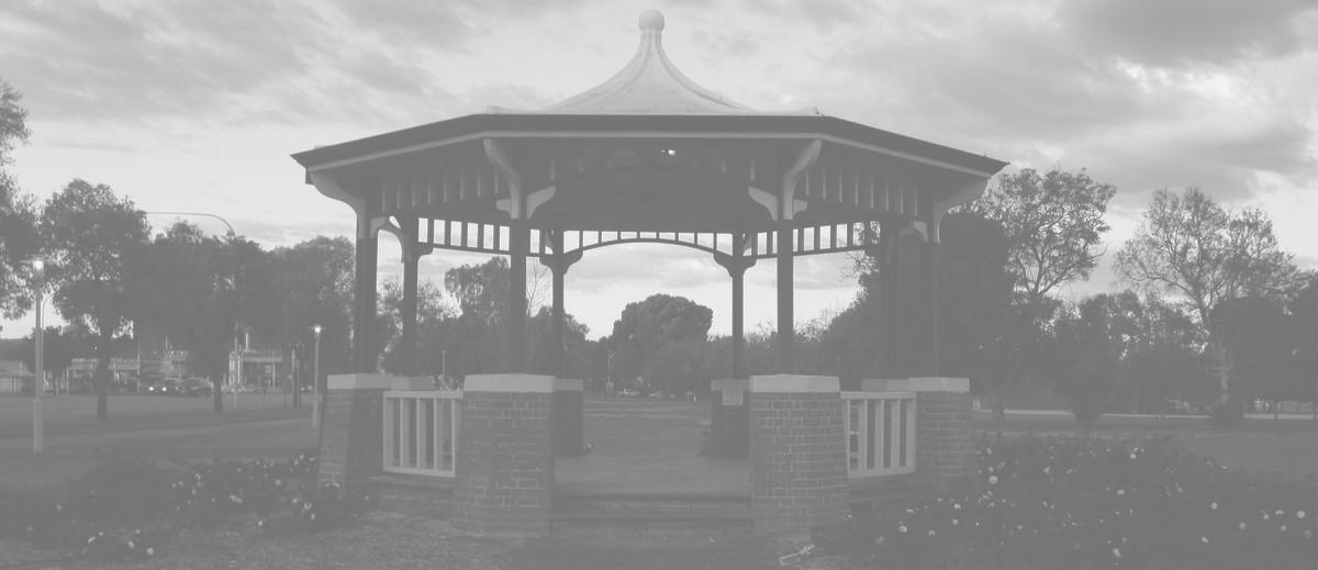 Image: A green and white gazebo with red brick footers stands in a park. A street with cars is visible in the left background