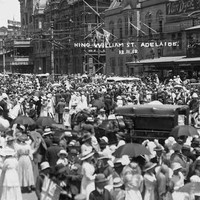 Image: a huge crowd of men, women and children in early 20th century dress gather in a city street in celebration. Written on the photograph are the words "King William St, Adelaide: 12.11.18"