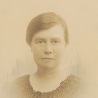 Image: A photographic head-and-shoulders portrait of a woman with ear-length dark hair and wearing 1920s attire