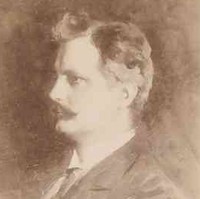 Image: A photographic head-and-shoulders portrait of a young man wearing a late-Victorian era suit and sporting a dark, handlebar moustache