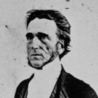 Image: Photographic portrait of a middle-aged Caucasian man in the clothing of a Christian minister. He is sitting in an high-backed chair and has his right hand resting on a book--possibly a bible