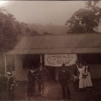 Image: group of people in front of small building displaying banner