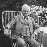 Image: An elderly man with a cane sits in a chair within a garden